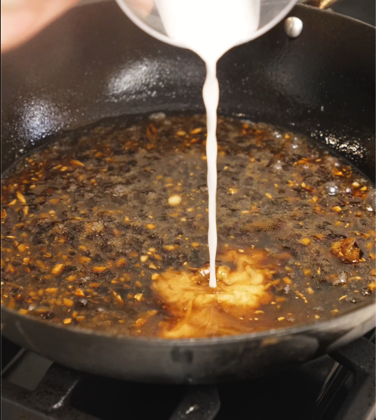 Cornstarch slurry being poured into the simmering teriyaki sauce as it thickens into a glossy, sticky consistency.