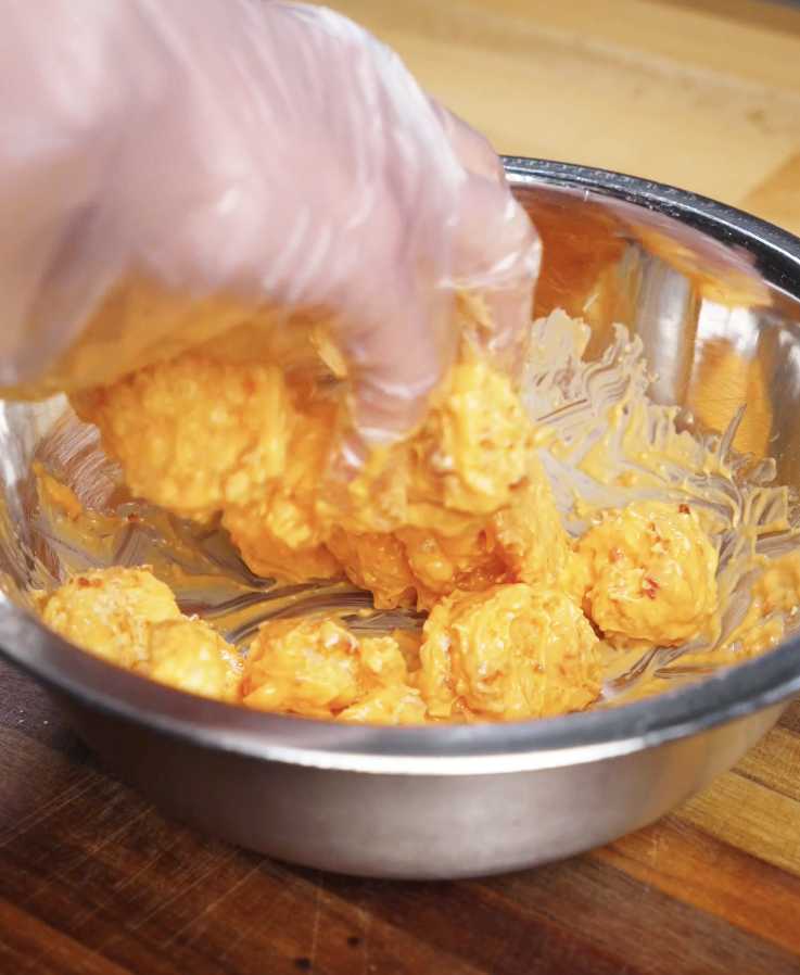 Air-fried shrimp being tossed in a bowl with creamy bang bang sauce until evenly coated, creating the signature sweet-spicy finish.