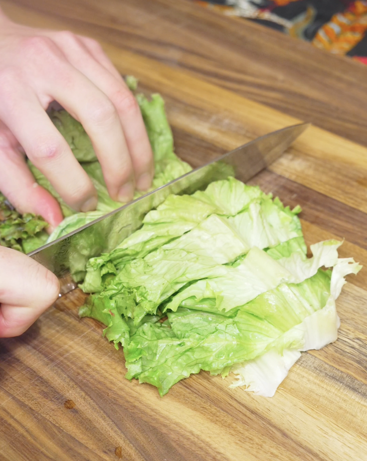 Chopping fresh red lettuce on a wooden cutting board to prepare the crisp vegetable base for a Thai beef salad, adding crunch and freshness to the dish.