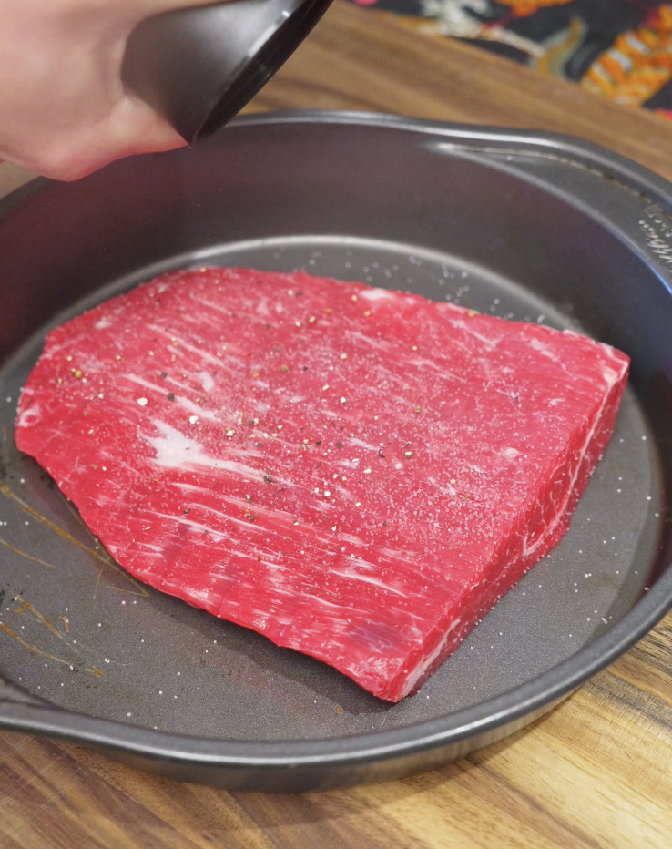 Seasoning raw flank steak with salt and black pepper before searing, preparing the protein for a healthy Thai beef salad.