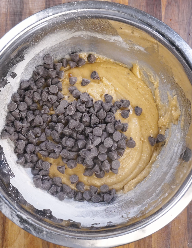 Dark chocolate chips scattered over brown butter cookie dough before folding in for even chocolate distribution.
