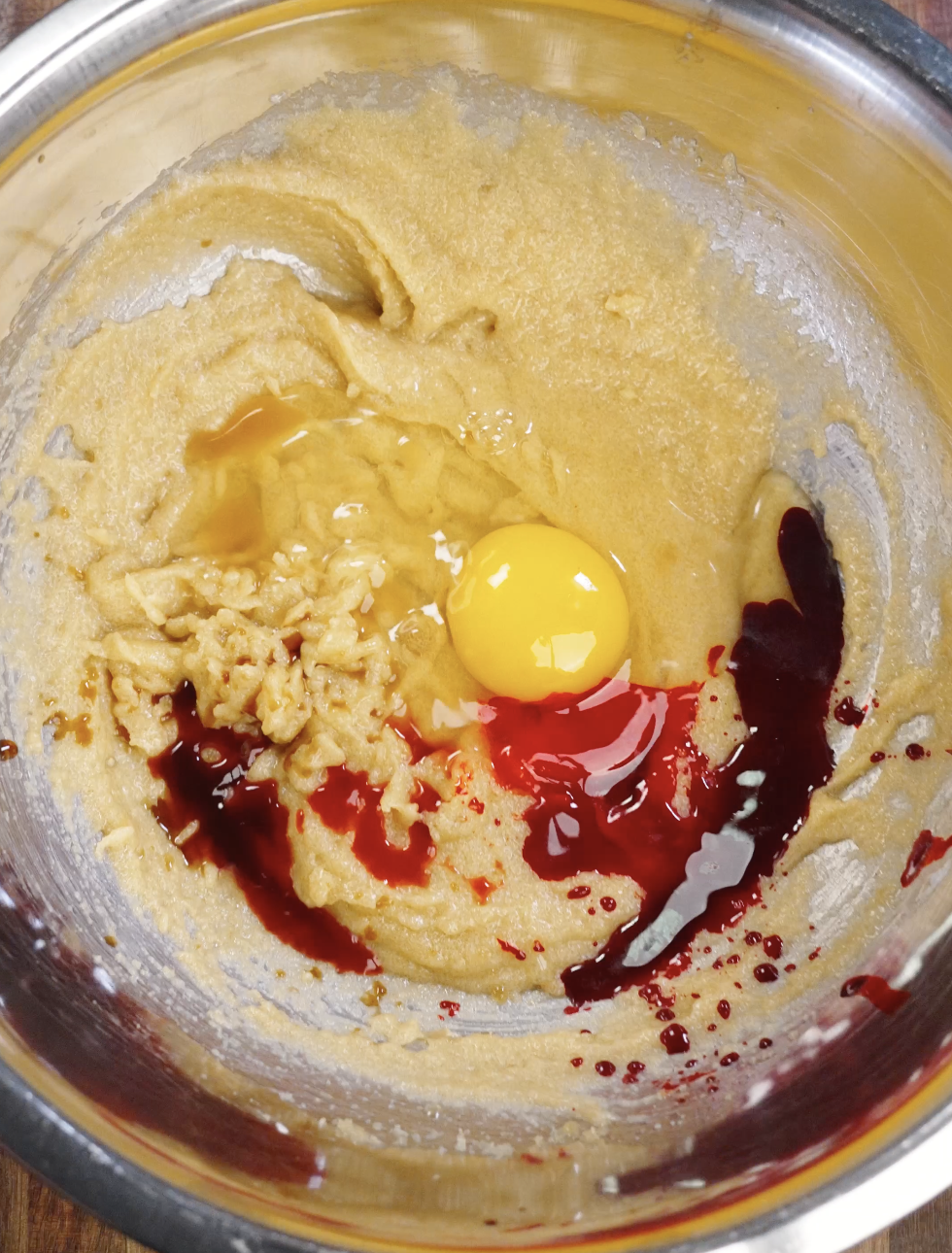 Egg, vanilla extract, white vinegar, and red food coloring added to the creamed butter and sugar mixture to build the signature red velvet flavor and texture.