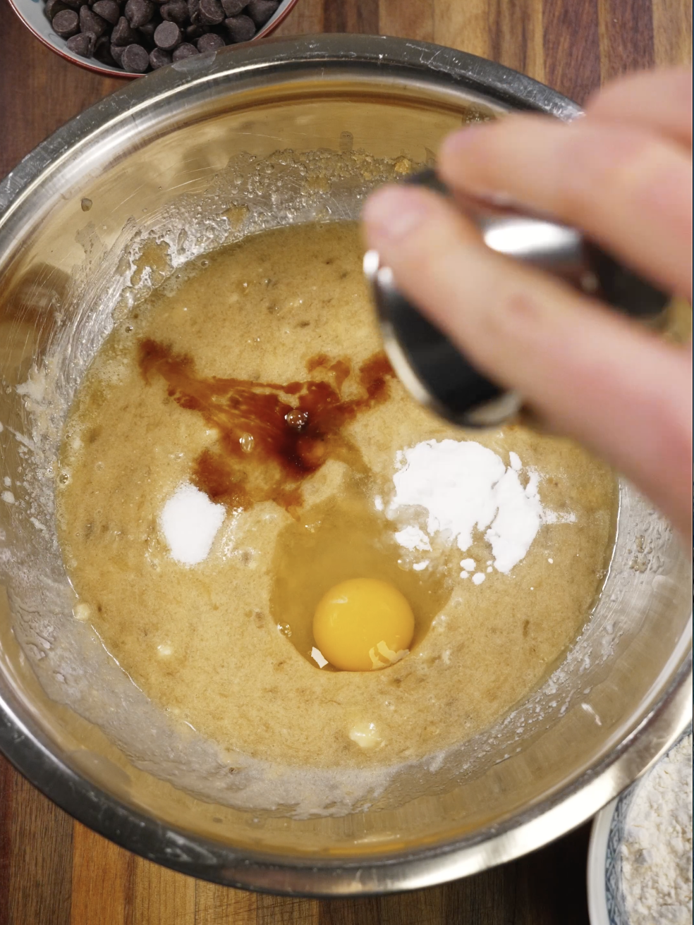 Egg, vanilla extract, salt, and baking soda added to banana bread batter in a mixing bowl, building flavor and structure for a tender banana bread loaf.