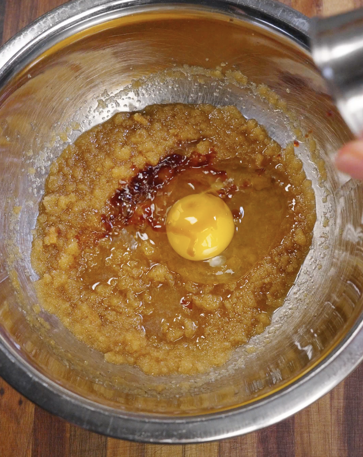 Egg cracked into a bowl of brown butter and sugar, creating a glossy mixture for double chocolate cookie dough.