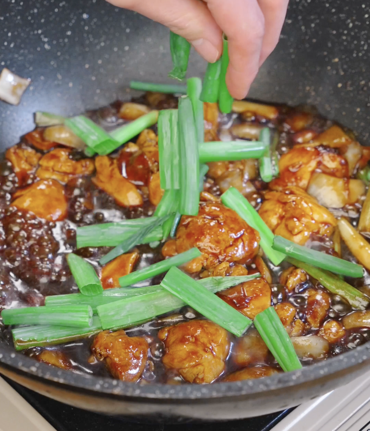 Fresh scallion greens being sprinkled over the simmering chicken and onion stir fry just before finishing the dish.