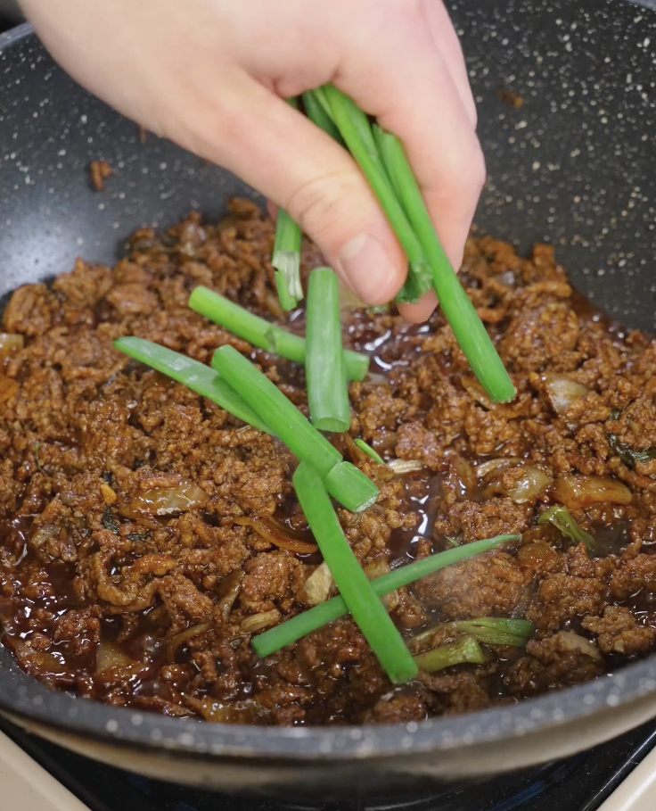 Fresh scallion greens being added to simmering black pepper ground beef in a skillet just before finishing the dish.
