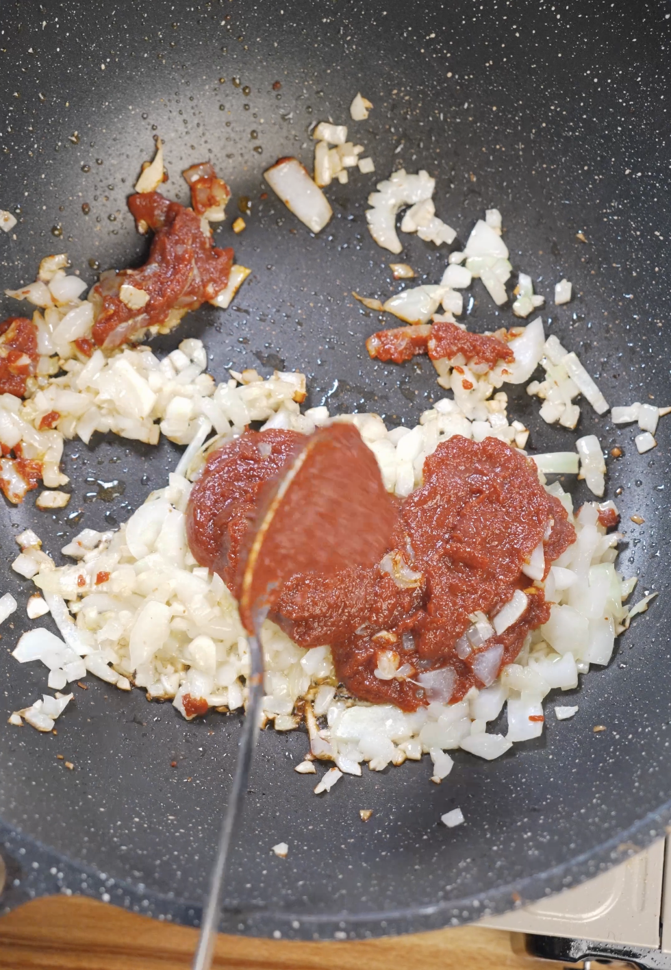 Tomato paste spooned into saut&eacute;ed onions and garlic in a pan, beginning the process of cooking it down until deep red for vodka sauce.