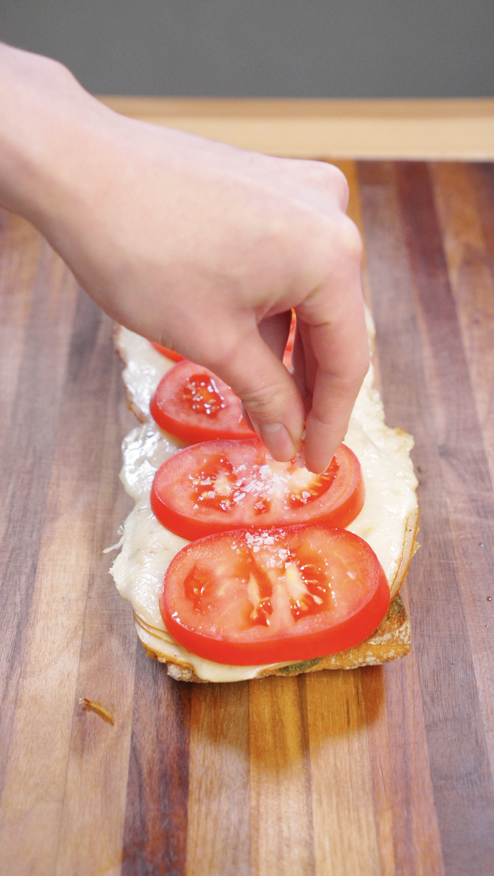 Fresh tomato slices placed on top of melted provolone and seared turkey on toasted ciabatta bread while assembling a turkey pesto sandwich.