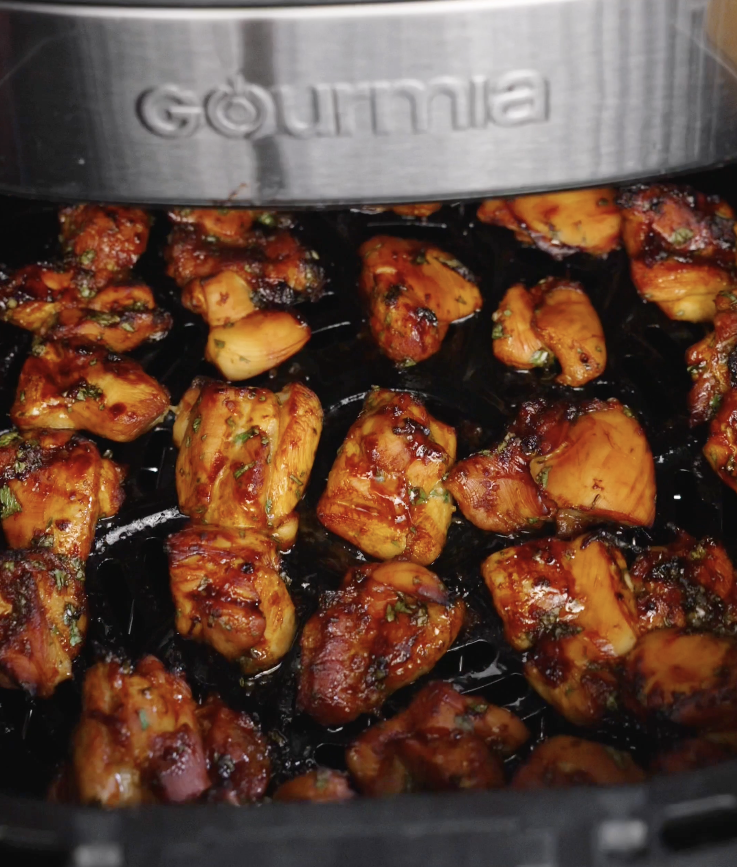 Sticky Cilantro Chicken pieces caramelized and lightly charred inside an air fryer basket after cooking, showing glossy honey soy glaze and flecks of cilantro.