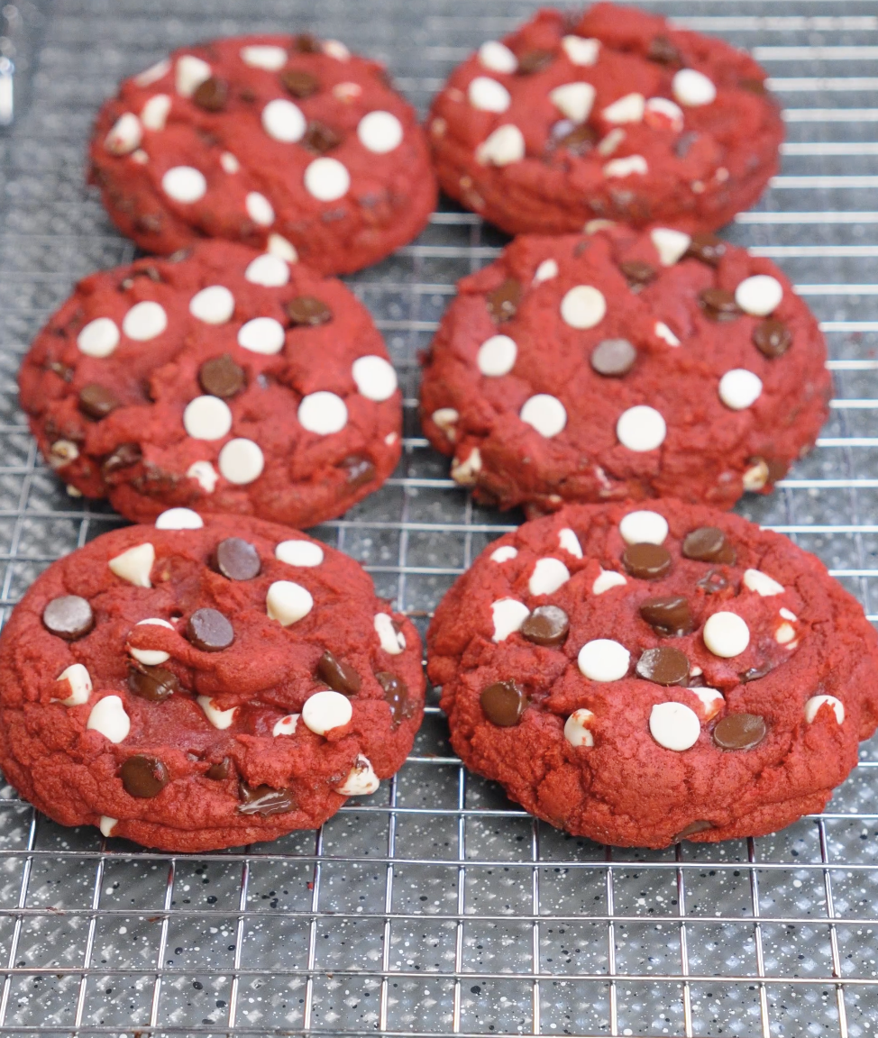 Freshly baked red velvet cookies with crisp edges and soft centers resting on a cooling rack, topped with white and dark chocolate chips