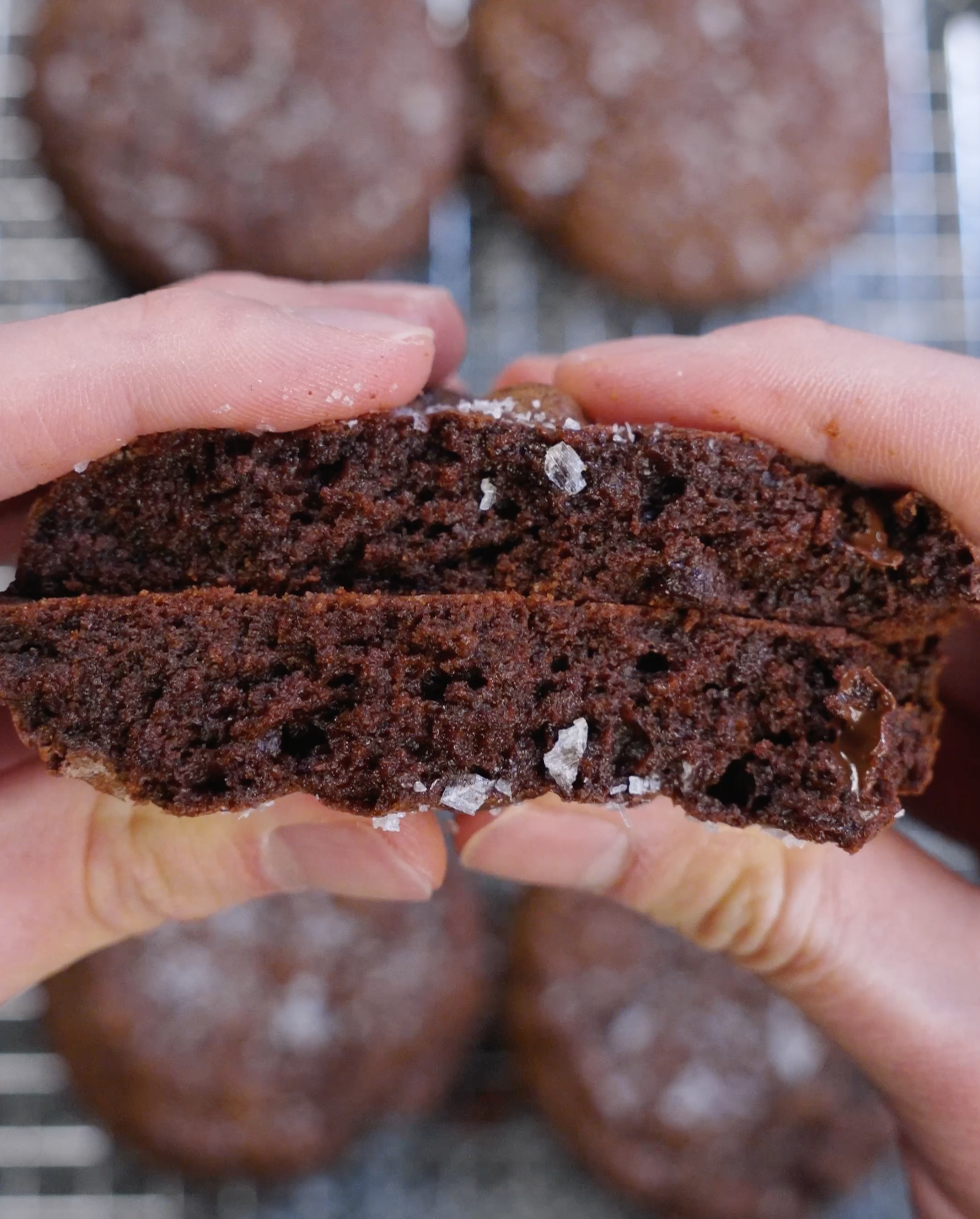 Brownie cookie split in half to show a rich, moist, fudgy interior with deep chocolate crumb and melted chocolate throughout.