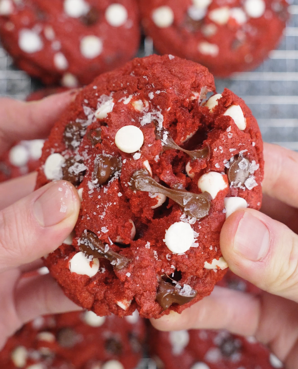 Red velvet cookie being pulled apart to reveal a soft, gooey center with melted chocolate chips and tender crumb texture.