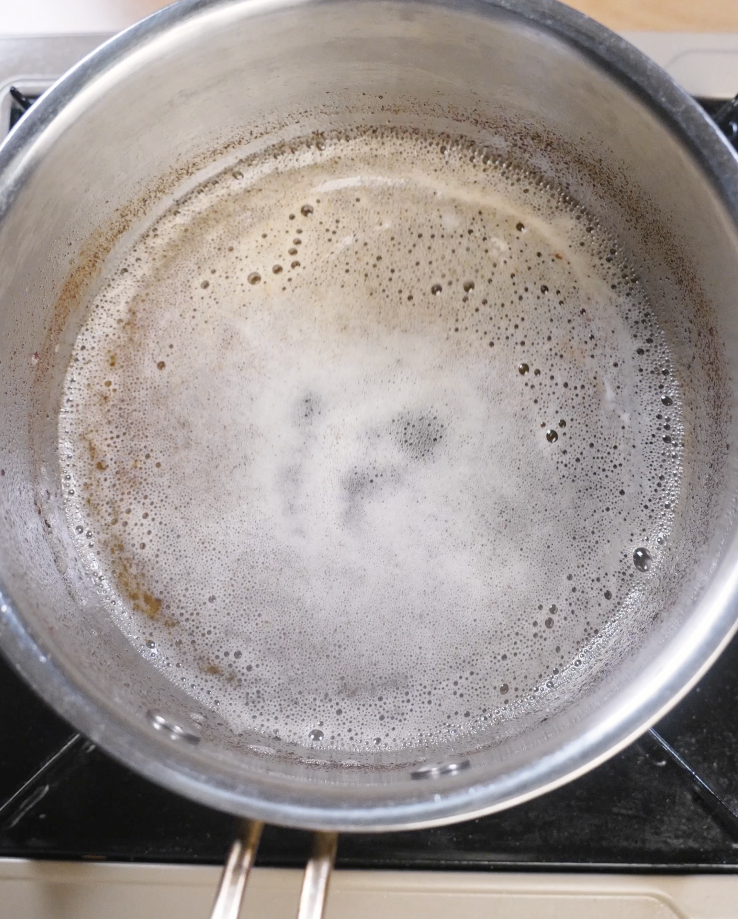Unsalted butter melting and foaming in a saucepan over medium heat as the milk solids begin to brown, creating nutty brown butter for chocolate chip cookies.