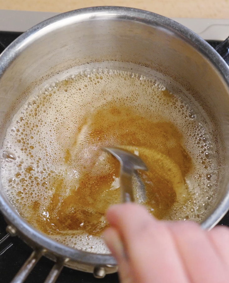 Unsalted butter browning in a saucepan until amber with foamy bubbles and toasted milk solids for double chocolate brown butter cookies.
