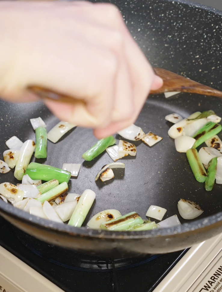 Onion chunks and scallion whites cooking in a skillet until lightly charred to build flavor for Mongolian chicken.