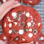 Detailed close up of a red velvet cookie packed with white chocolate chips and dark chocolate chips, highlighting its vibrant red color and crinkled top.