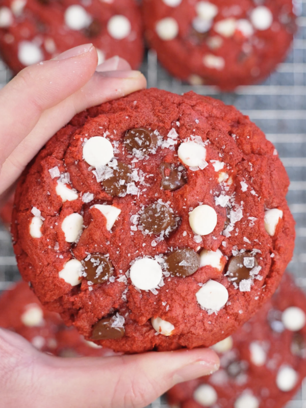 Detailed close up of a red velvet cookie packed with white chocolate chips and dark chocolate chips, highlighting its vibrant red color and crinkled top.