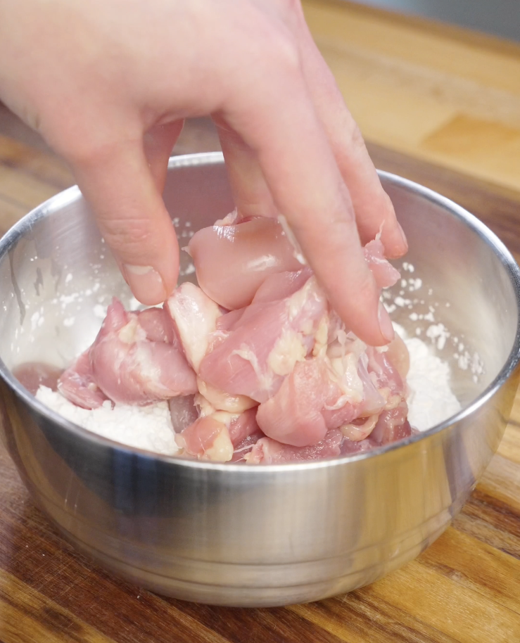 Bite sized boneless skinless chicken thighs being tossed in cornstarch and salt to create a crispy coating for air fryer bang bang chicken.