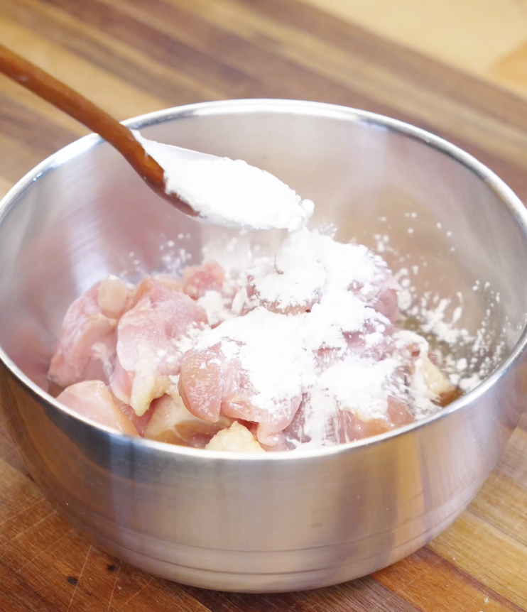 Bite sized chicken thigh pieces tossed with cornstarch in a mixing bowl to create a light velveting coating that keeps the chicken tender in Chicken Onion Stir Fry.