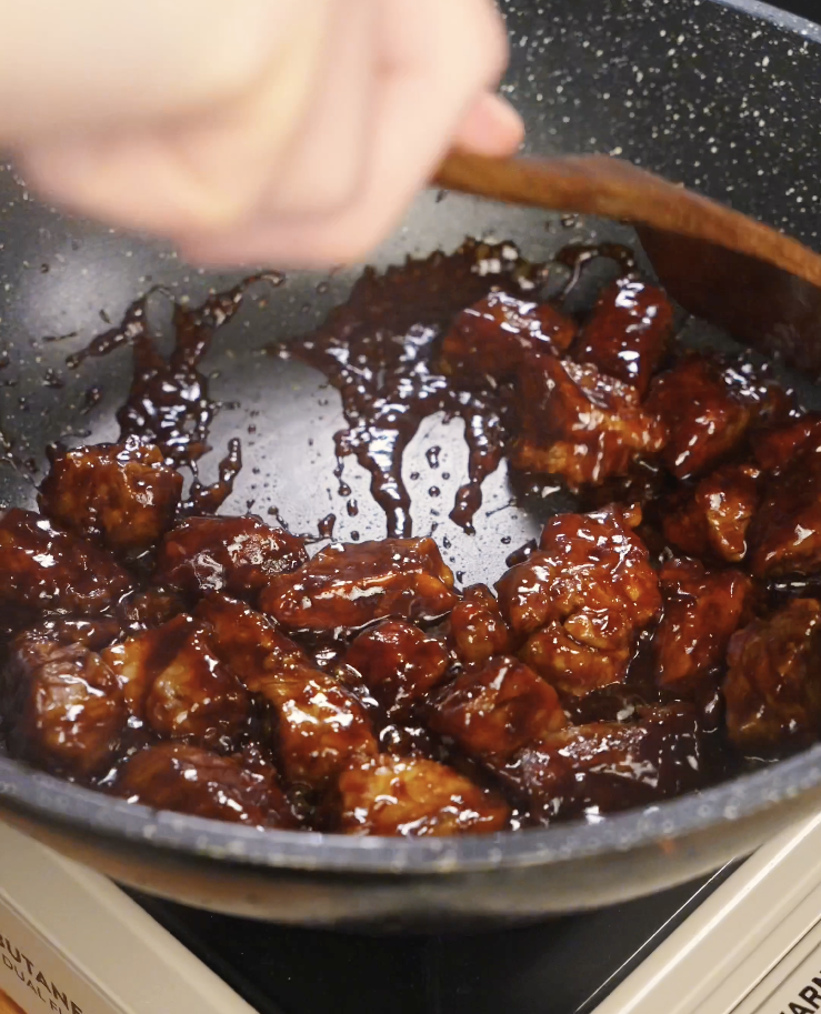 Beef cubes simmering in a thickened soy garlic sauce inside a pan, with the glossy glaze coating each piece as the sauce reduces and caramelizes.