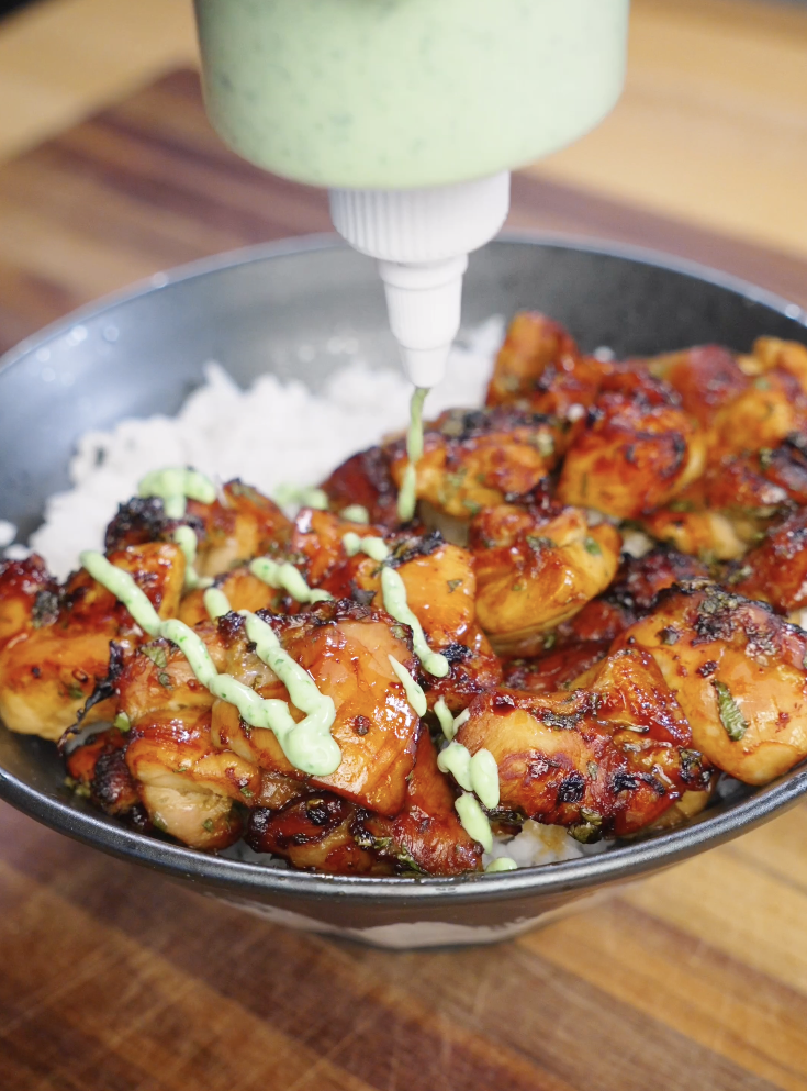 Cilantro cream being squeezed over air fried Sticky Cilantro Chicken served on white rice, creating a creamy green drizzle over caramelized chicken pieces.