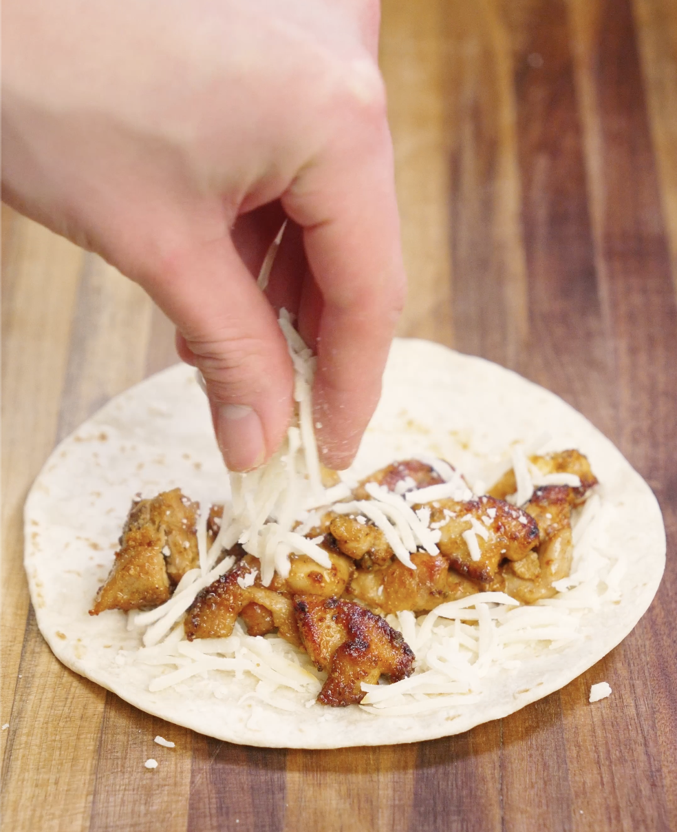 Crispy pan-seared chicken pieces placed onto a warm flour tortilla with shredded cheese, forming the base of homemade crispy chicken tacos.