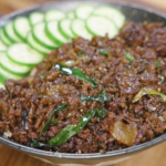 Black pepper ground beef served over rice in a bowl, topped with sautéed scallions and sliced cucumbers arranged along the edge for a complete rice bowl.