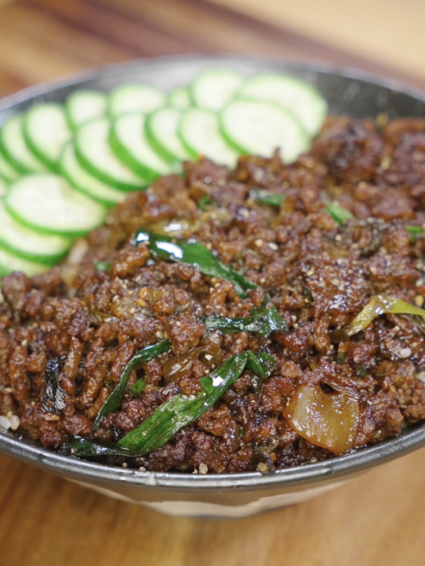 Black pepper ground beef served over rice in a bowl, topped with sautéed scallions and sliced cucumbers arranged along the edge for a complete rice bowl.