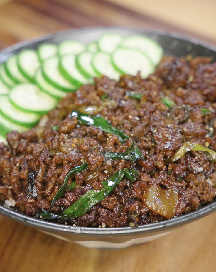 Black pepper ground beef served over rice in a bowl, topped with saut&eacute;ed scallions and sliced cucumbers arranged along the edge for a complete rice bowl.