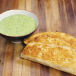 Golden brown crispy chicken tacos served on a wooden cutting board alongside a bowl of creamy cilantro mayo sauce, ready to eat.