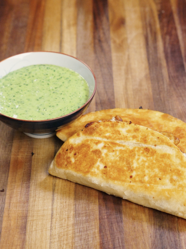 Golden brown crispy chicken tacos served on a wooden cutting board alongside a bowl of creamy cilantro mayo sauce, ready to eat.