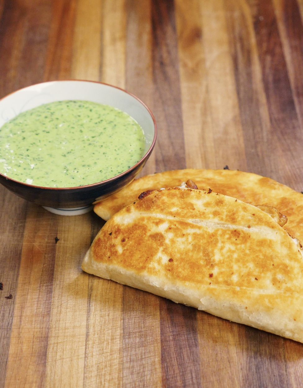 Golden brown crispy chicken tacos served on a wooden cutting board alongside a bowl of creamy cilantro mayo sauce, ready to eat.