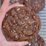 Thick double chocolate brown butter cookies baked until set with cracked tops, melted chocolate puddles, and flaky sea salt on a cooling rack.