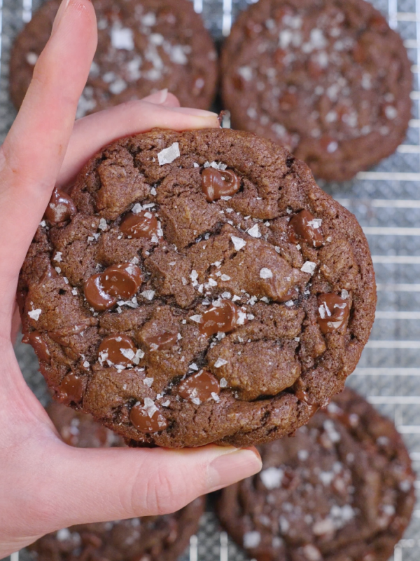 Thick double chocolate brown butter cookies baked until set with cracked tops, melted chocolate puddles, and flaky sea salt on a cooling rack.