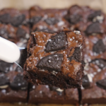 A thick fudgy Oreo brownie square lifted with a fork, showing a crackly top, embedded Oreo pieces, and a dense chocolate interior.