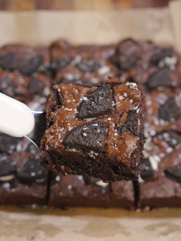 A thick fudgy Oreo brownie square lifted with a fork, showing a crackly top, embedded Oreo pieces, and a dense chocolate interior.