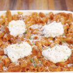 Baked vodka pasta topped with dollops of ricotta cheese, grated Parmesan, cracked black pepper, and chives, ready to be served straight from the oven.