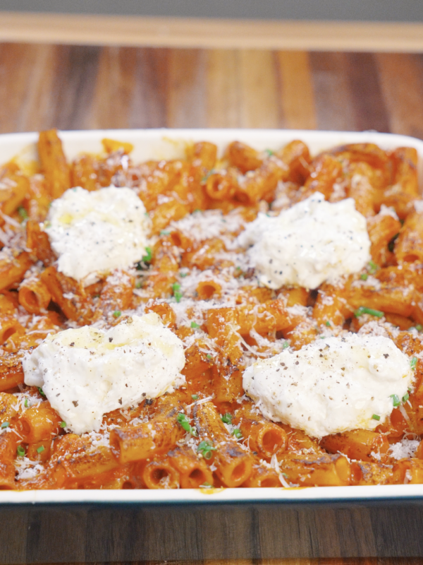 Baked vodka pasta topped with dollops of ricotta cheese, grated Parmesan, cracked black pepper, and chives, ready to be served straight from the oven.