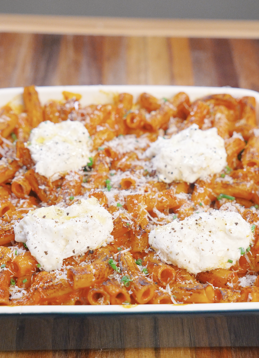 Baked vodka pasta topped with dollops of ricotta cheese, grated Parmesan, cracked black pepper, and chives, ready to be served straight from the oven.