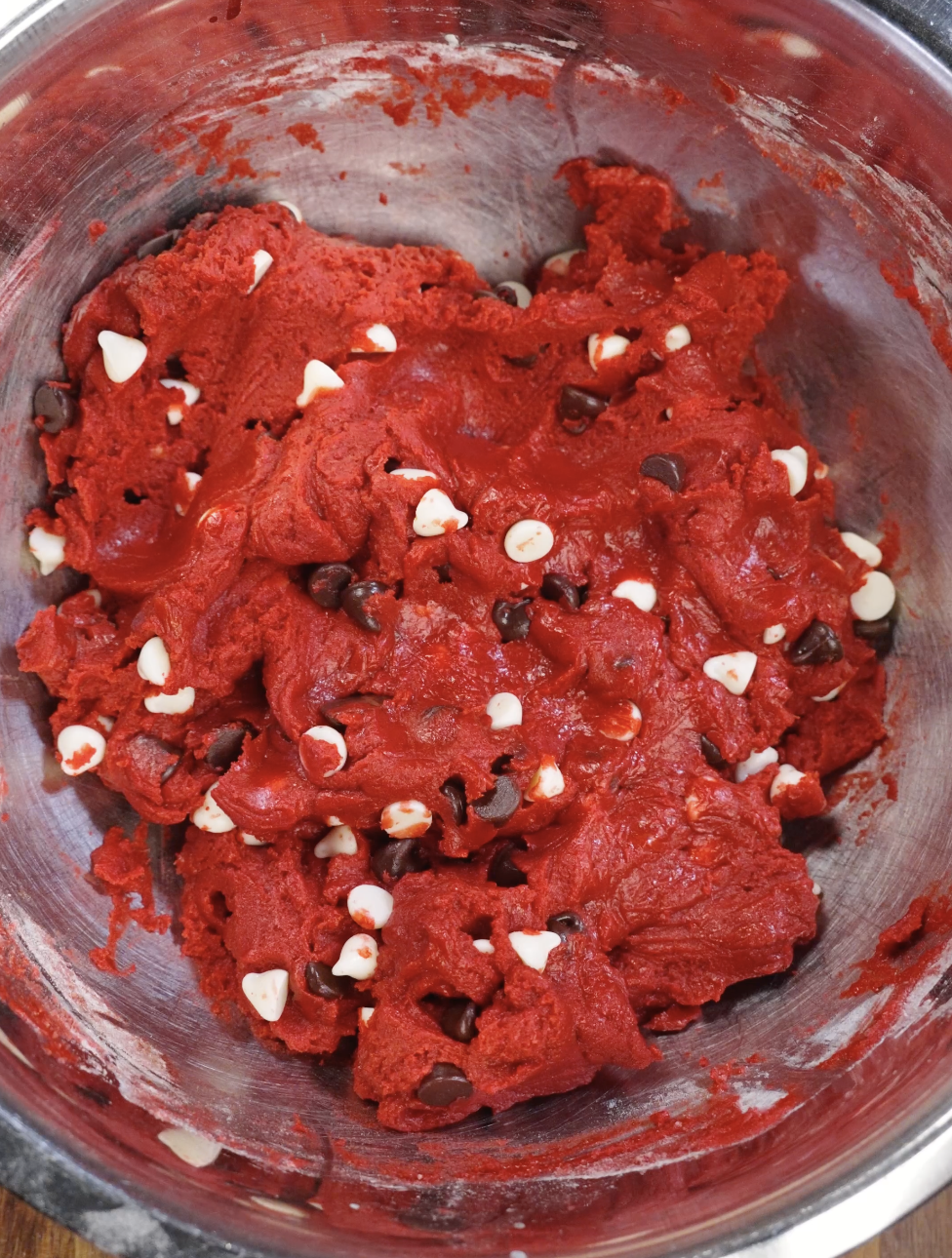 Thick red velvet cookie dough studded with dark and white chocolate chips after folding, showing evenly distributed chocolate throughout the batter.