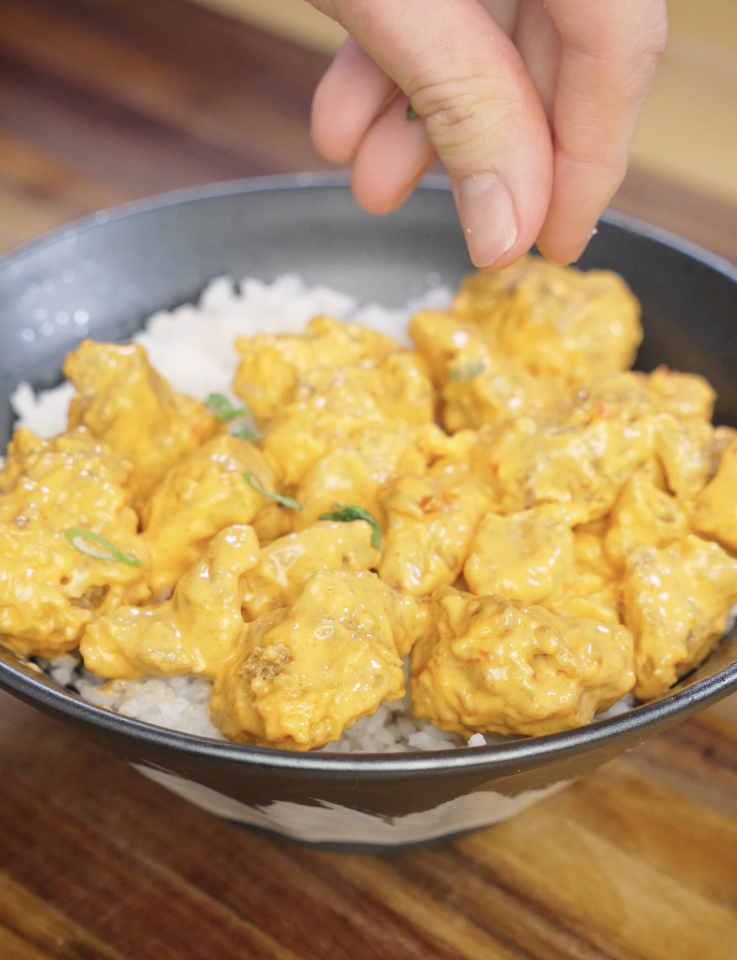 Fresh sliced scallions being sprinkled over bang bang chicken to add brightness and contrast to the creamy spicy sauce.