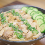 Finished bowl of ginger scallion chicken made with juicy poached chicken thighs shredded and tossed with soy sauce, topped with fragrant ginger scallion oil and served over white rice with fresh cucumber slices.