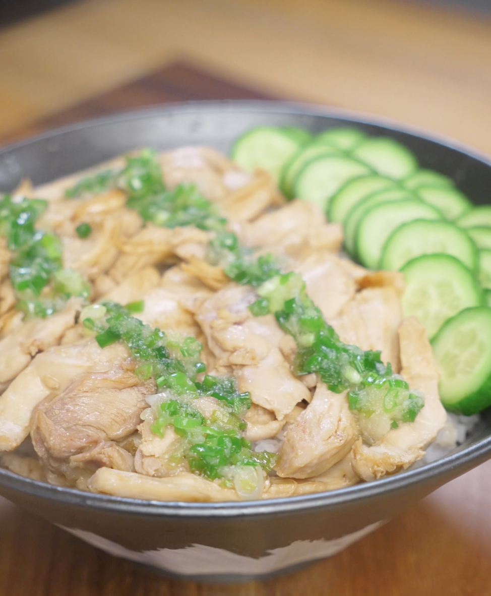 Finished bowl of ginger scallion chicken made with juicy poached chicken thighs shredded and tossed with soy sauce, topped with fragrant ginger scallion oil and served over white rice with fresh cucumber slices.