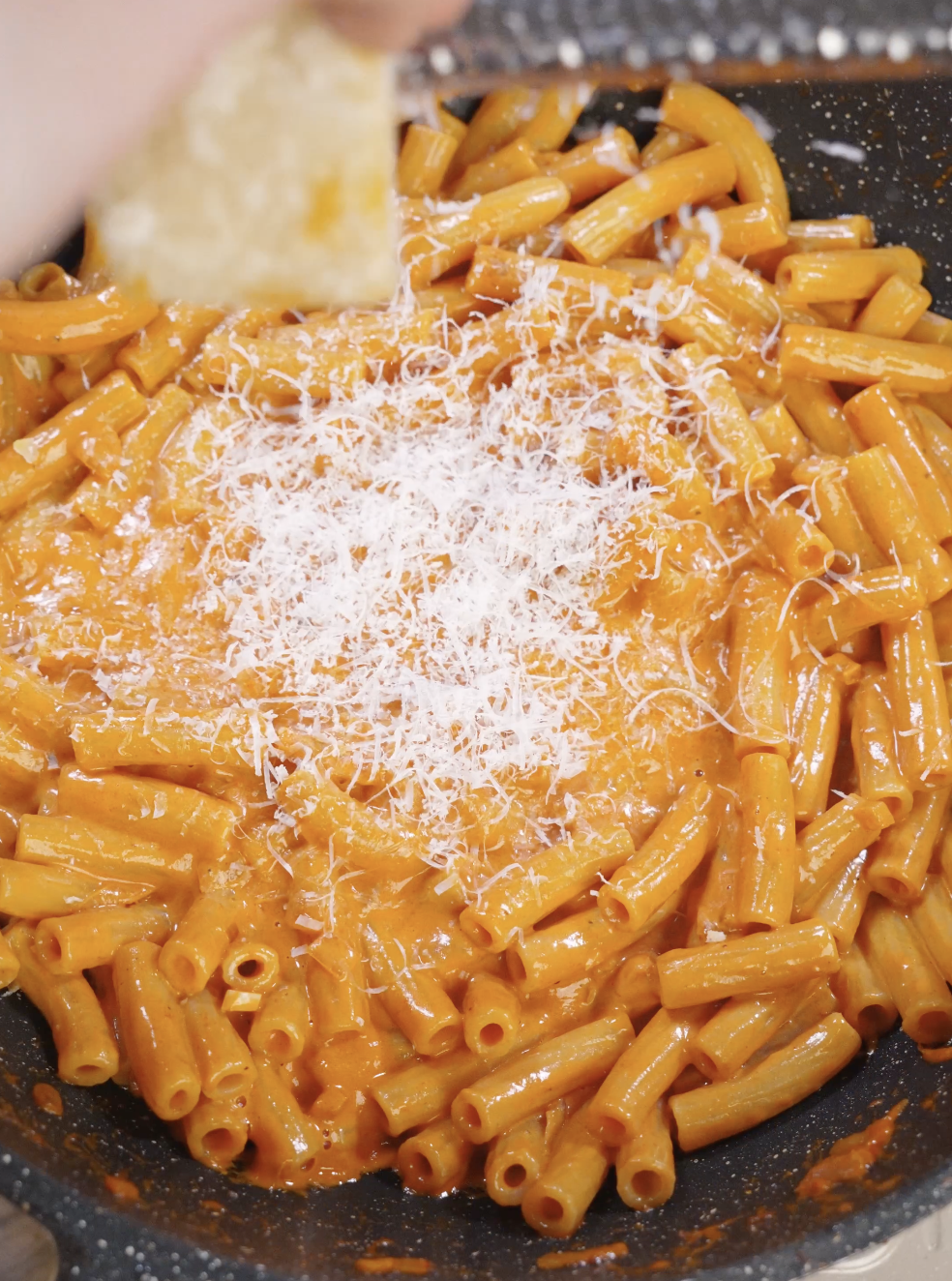 Freshly grated Parmesan cheese being sprinkled over rigatoni coated in creamy vodka sauce in a skillet, adding richness and finishing the pasta before baking or serving.