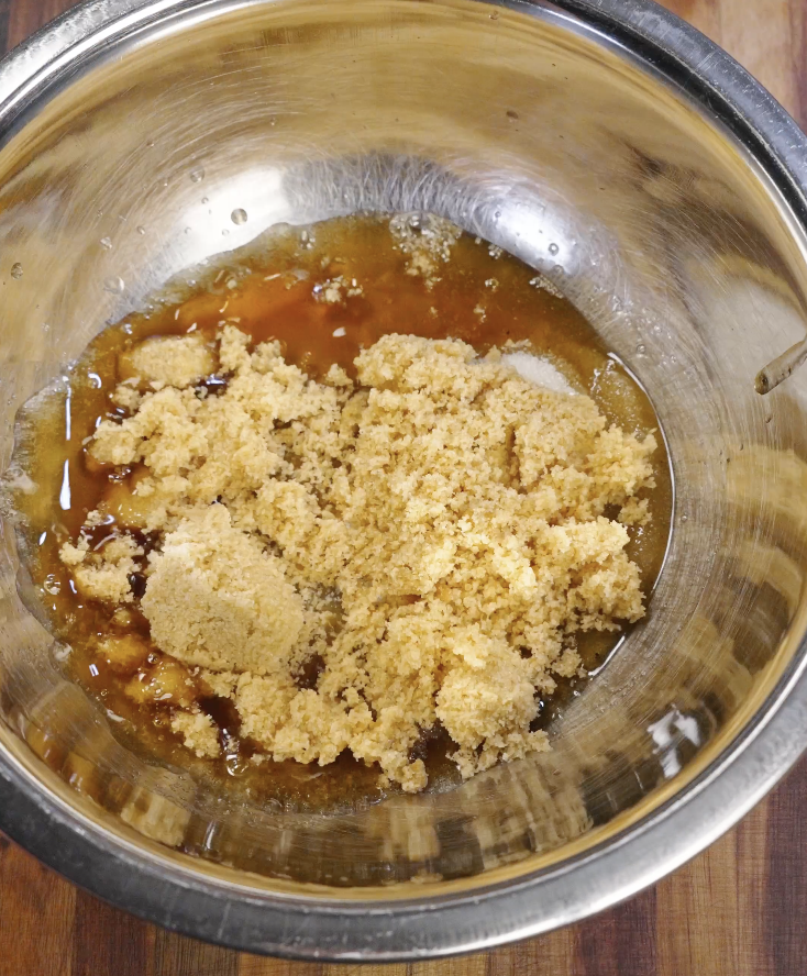 Brown sugar added to warm browned butter in a mixing bowl, beginning the base for double chocolate brown butter cookie dough.