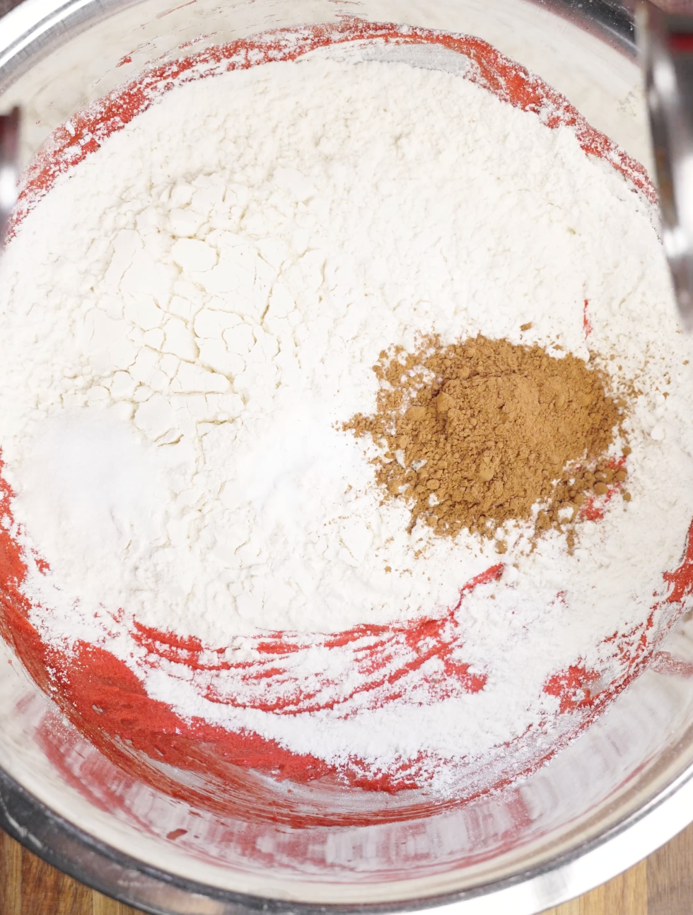 Mixing Cocoa Powder and Flour into Red Velvet Cookie Dough Alt Text: Cocoa powder and all purpose flour layered over bright red cookie dough before being gently folded to prevent overmixing and maintain soft centers.