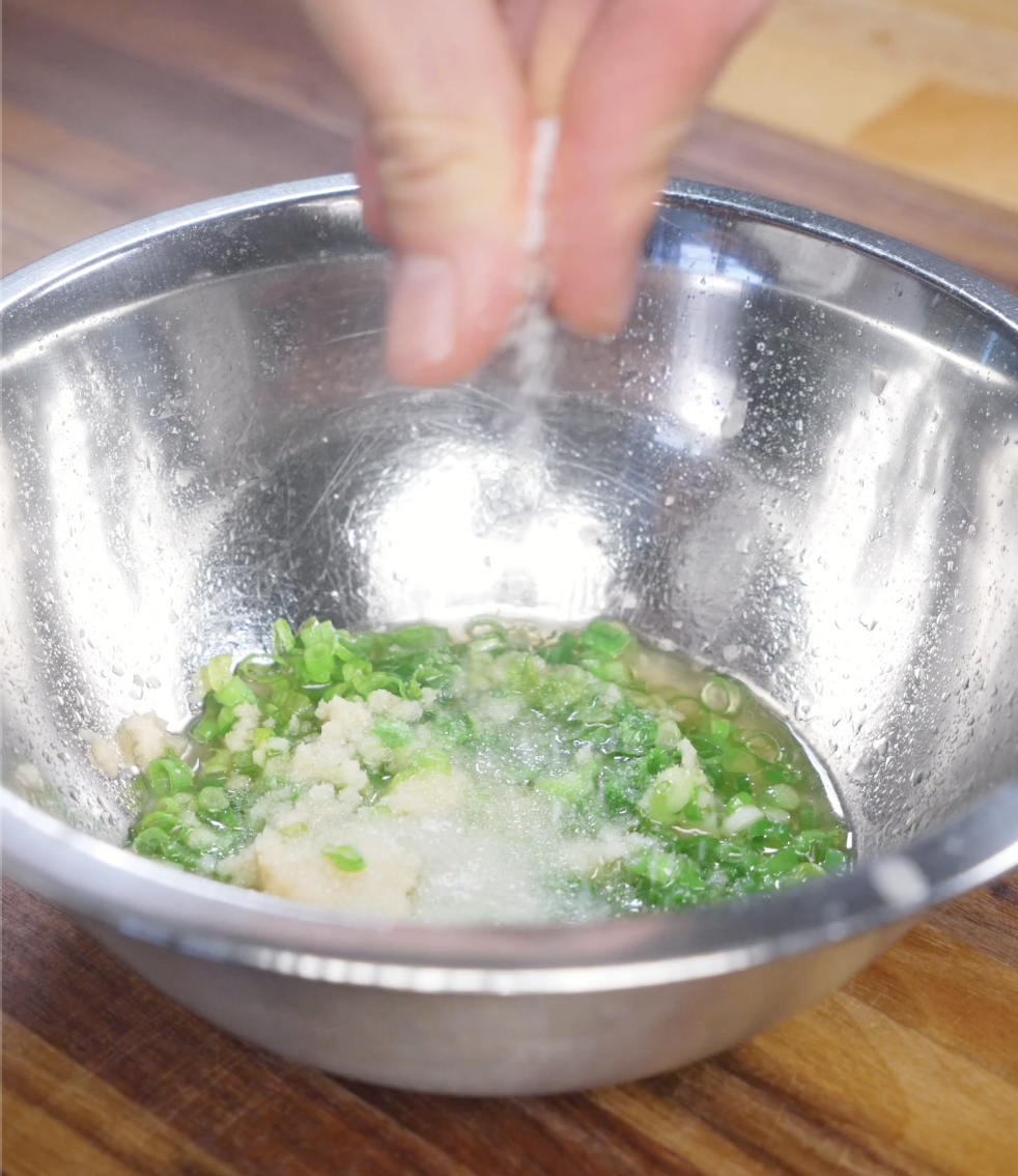 Finely chopped scallions and grated ginger combined in a stainless steel bowl as the base for classic ginger scallion sauce.