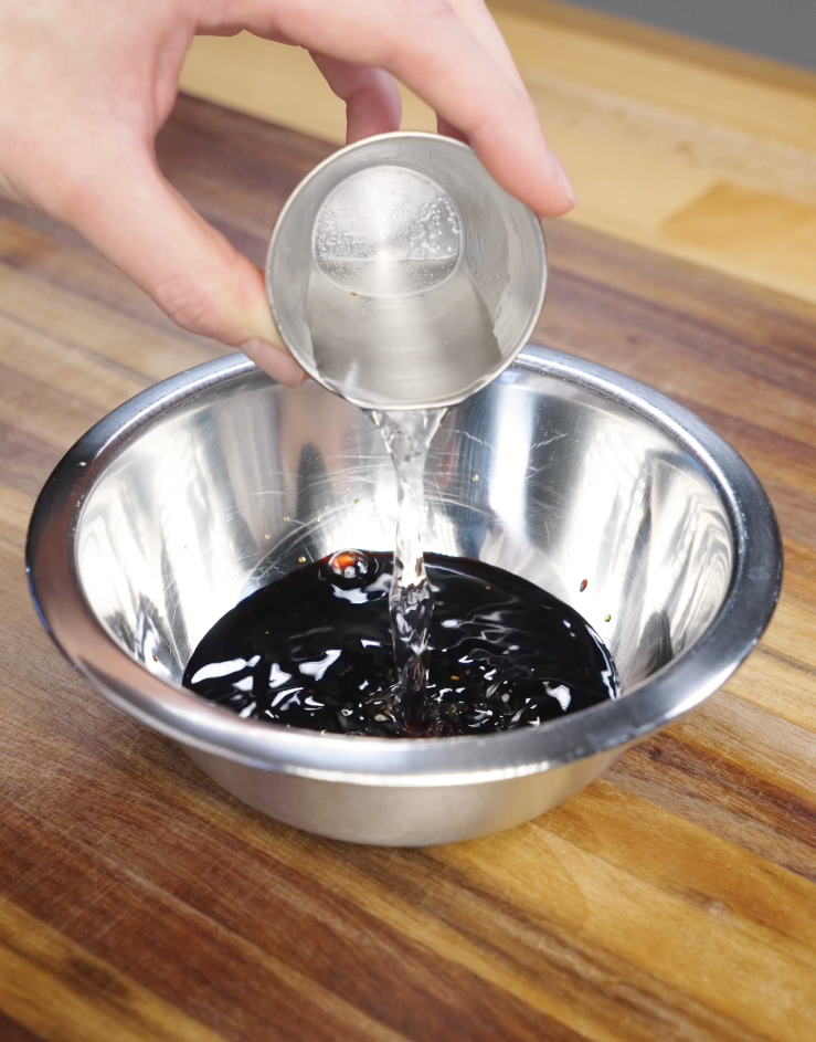 Water being poured into a bowl with dark soy sauce, light soy sauce, dashi powder, and sugar to create the sweet umami Mongolian chicken sauce.