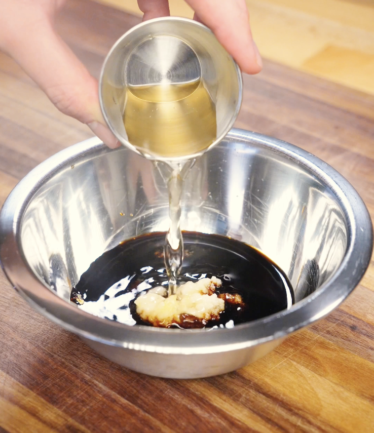 Soy garlic sauce being mixed in a stainless steel bowl with dark soy sauce, light soy sauce, oyster sauce, minced garlic, sugar, and vinegar, creating a glossy sweet and savory glaze for soy garlic beef.