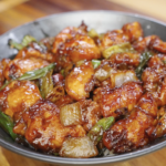 Finished Mongolian chicken tossed in a thick sweet and savory soy sauce with caramelized onions and scallions served over steamed rice.